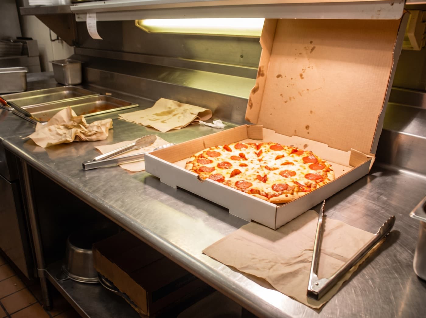 The same pizza after enhancement: warm neutral light, visible crust and cheese texture, tidy counter.