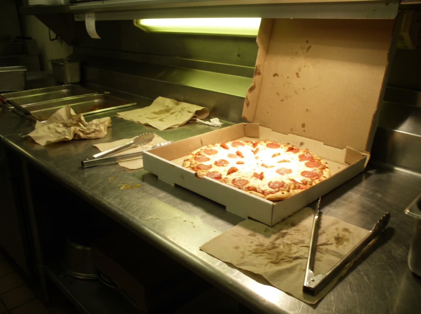 A pizza photographed on a phone under kitchen fluorescent lighting: dim, green colour cast, blown-out highlights.